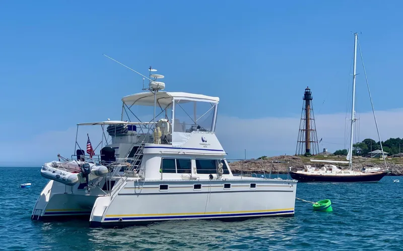 Tranquility Base Yacht Photos Pics 2003 PDQ-34 catamaran anchored near lighthouse, clear blue sky, and calm sea.