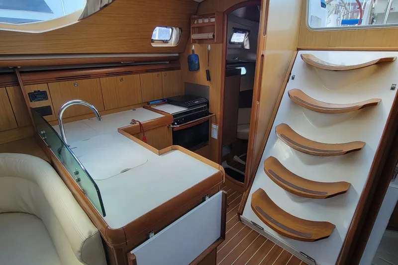  Yacht Photos Pics Interior of 2008 Jeanneau Sun Odyssey 42 DS yacht, featuring a compact kitchen and wooden stairs.