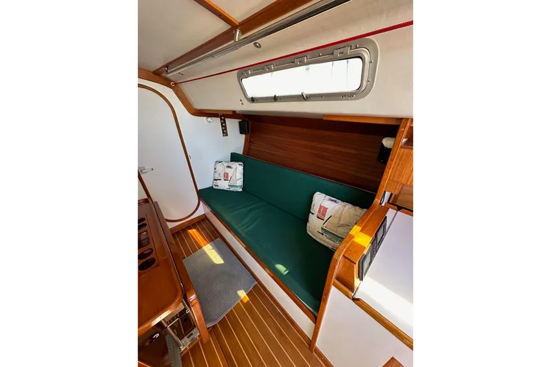 Ma Jolie Yacht Photos Pics 1996 J Boats J/120 interior with green cushioned seating, wooden accents, and nautical-themed pillows.