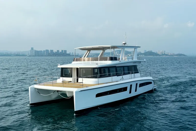  Yacht Photos Pics 2025 Mazarin 55 EVO II yacht cruising on open water with city skyline backdrop.