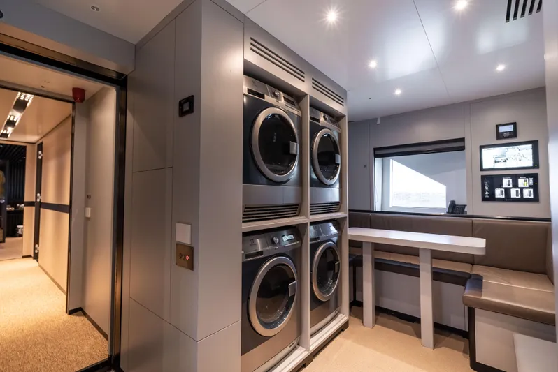 K+ Yacht Photos Pics Modern laundry room with stacked washers and dryers, seating area, and control panel.