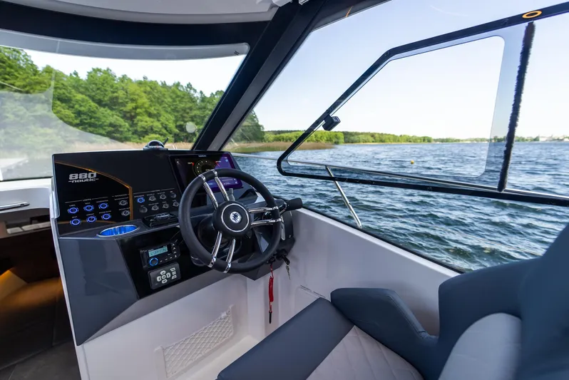  Yacht Photos Pics Modern Nautic 880 boat interior, 2025 model, featuring sleek dashboard and steering wheel, overlooking serene waters.