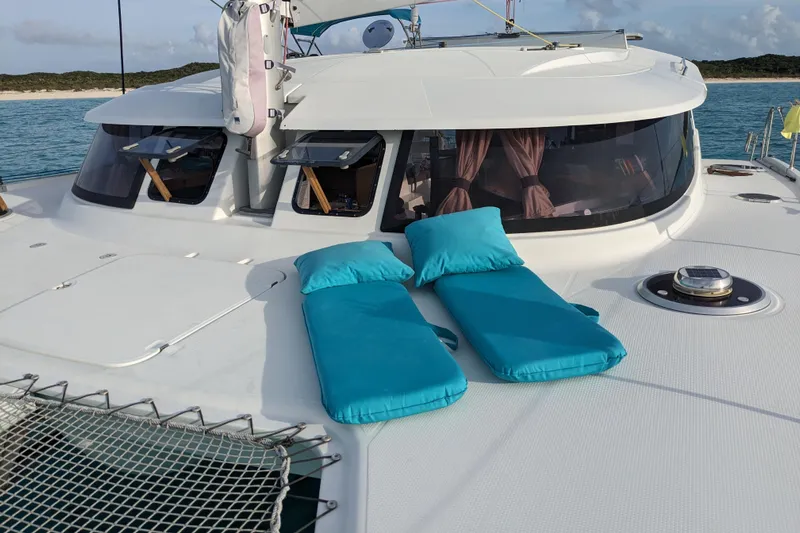 Imany Yacht Photos Pics 2012 Fountaine Pajot Lipari catamaran with turquoise cushions on deck, anchored near a scenic coastline.