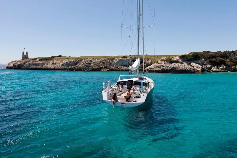  Yacht Photos Pics Sailing yacht Beneteau Sense 55, 2013 model, anchored in clear turquoise waters near rocky coastline.