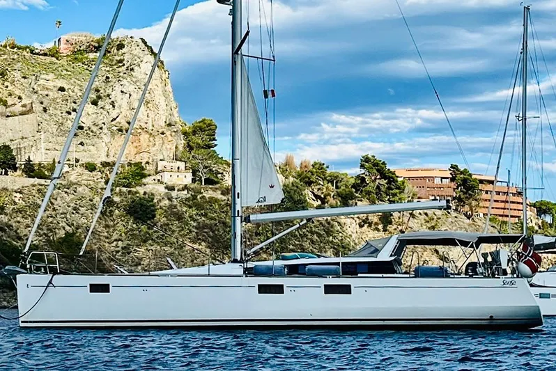  Yacht Photos Pics 2013 Beneteau Sense 55 sailboat anchored near rocky coastline under blue sky.