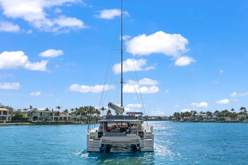 Halcyon Yacht Photos Pics 2024 Fountaine Pajot Aura 51 Catamaran sailing on a sunny day, surrounded by waterfront homes.