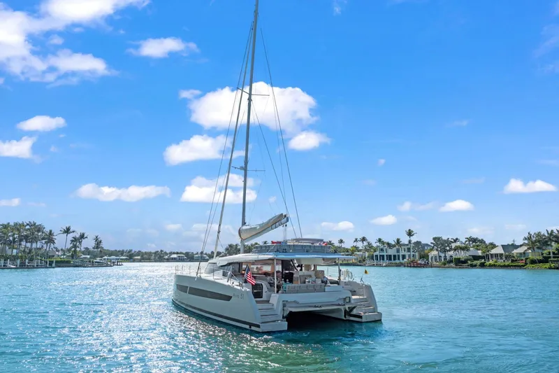 Halcyon Yacht Photos Pics 2024 Fountaine Pajot Aura 51 Catamaran sailing on a sunny day, surrounded by palm trees.