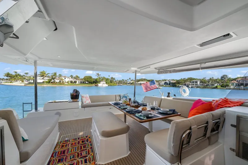 Halcyon Yacht Photos Pics Luxurious 2024 Fountaine Pajot Aura 51 Catamaran with elegant outdoor dining area and scenic waterfront view.