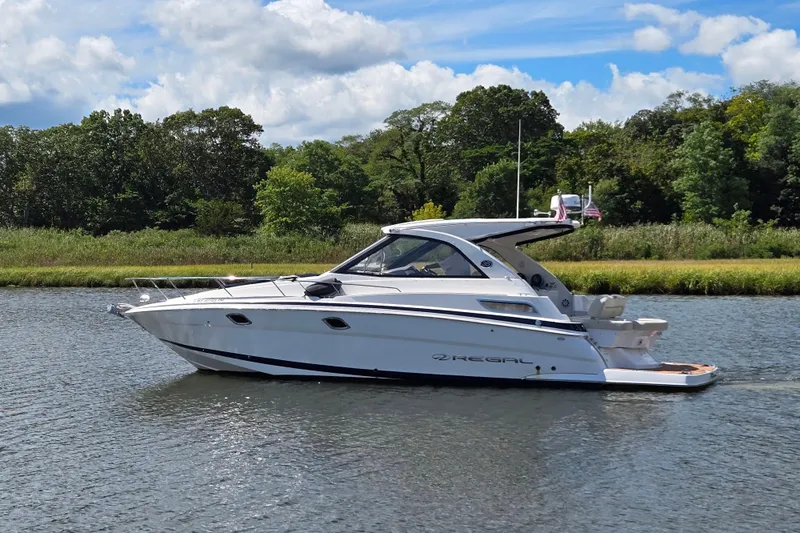  Yacht Photos Pics 2018 Regal 35 Sport Coupe boat cruising on a calm river with lush greenery.