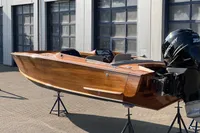 2024 Custom Bowrider boat with wooden finish and Mercury outboard motor, displayed on stands.