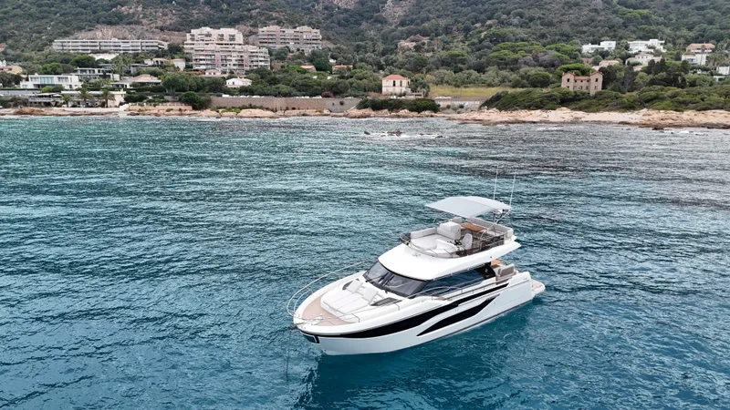 Prestige F4.9 Yacht Photos Pics Luxurious 2025 Prestige F4 yacht cruising near scenic coastline with lush greenery and modern buildings.