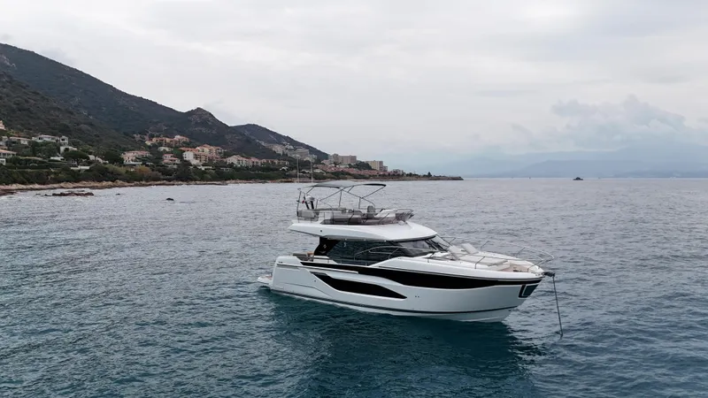 Prestige F4.9 Yacht Photos Pics 2025 Prestige F4 yacht anchored near a scenic coastline under a cloudy sky.