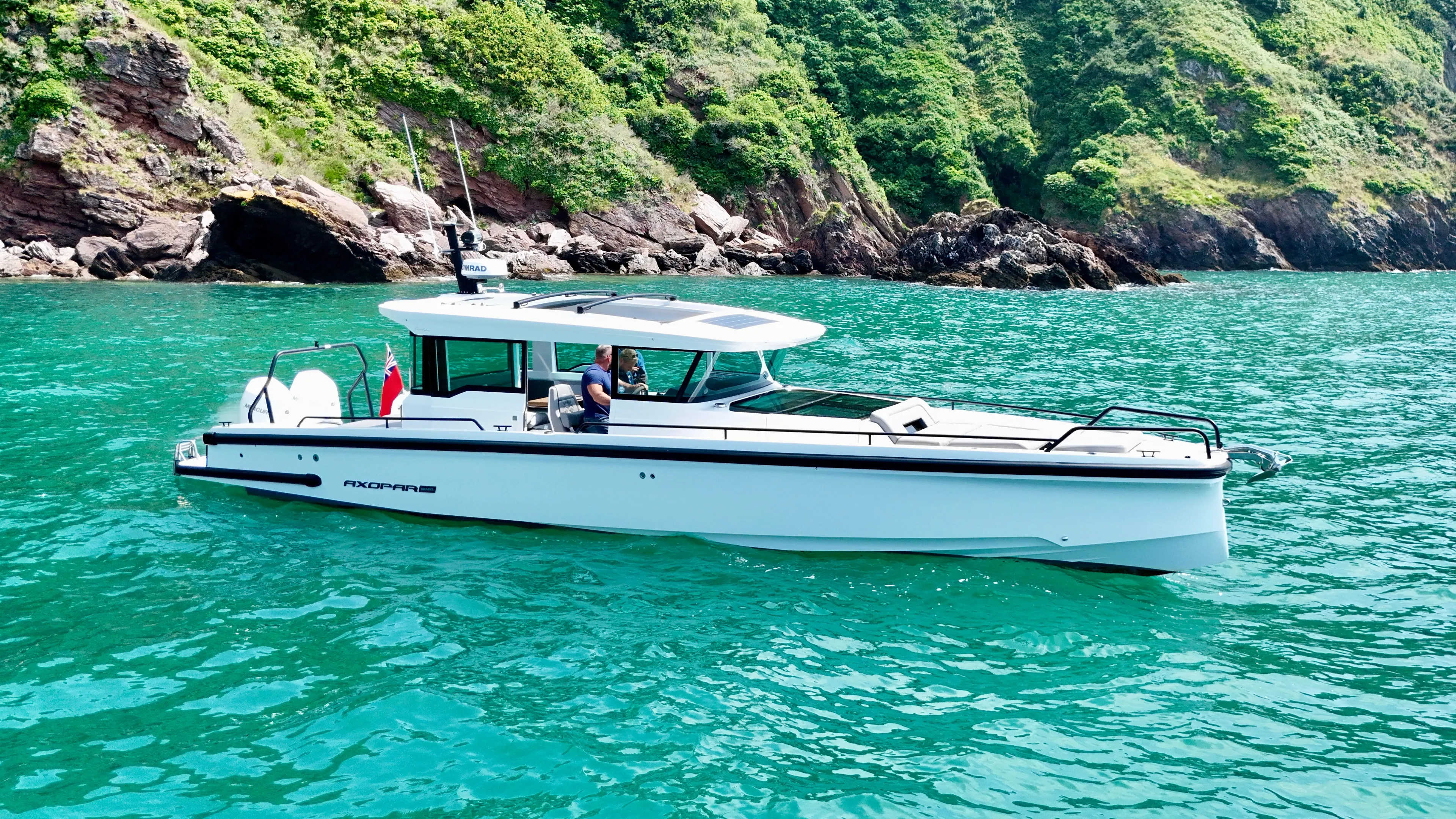 2020 Axopar 37 Cross Cabin boat on turquoise water near rocky coastline.