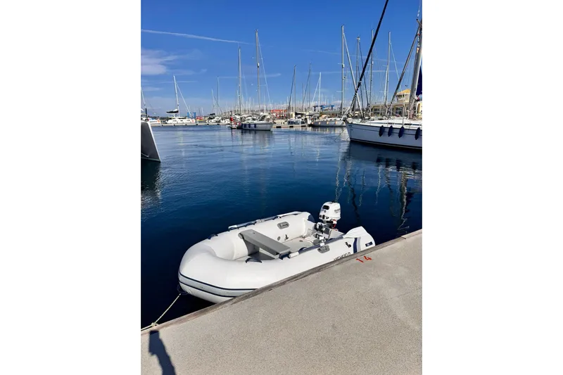 Searenity Yacht Photos Pics Inflatable dinghy moored at marina with sailboats, clear blue sky, and calm water.