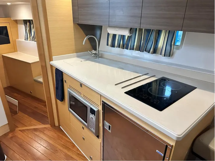  Yacht Photos Pics 2013 Pursuit 365i Sport Coupe interior kitchen with stove, microwave, and wood cabinetry.