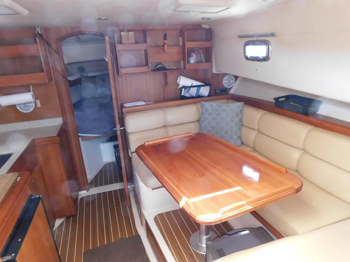 Calm Yacht Photos Pics 2005 Mainship 34 Rum Runner interior with wooden table, beige seating, and cozy cabin layout.