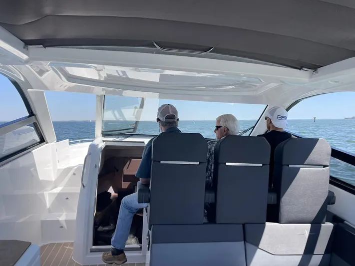 Inventory Clearance Yacht Photos Pics Three people seated inside a 2023 Bavaria Vida 33 boat, enjoying a scenic ocean view.