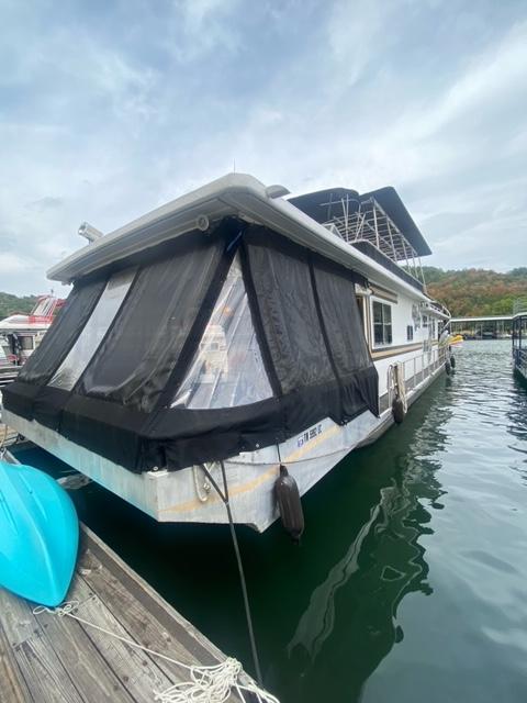 1985 Arc houseboat docked on calm water, featuring black window covers.