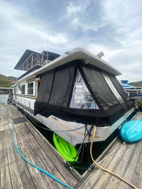 1985 Arc houseboat docked with covered deck and kayaks, under cloudy sky.