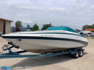 1999 Crownline 266 CCR boat on trailer, teal cover, parked outdoors.