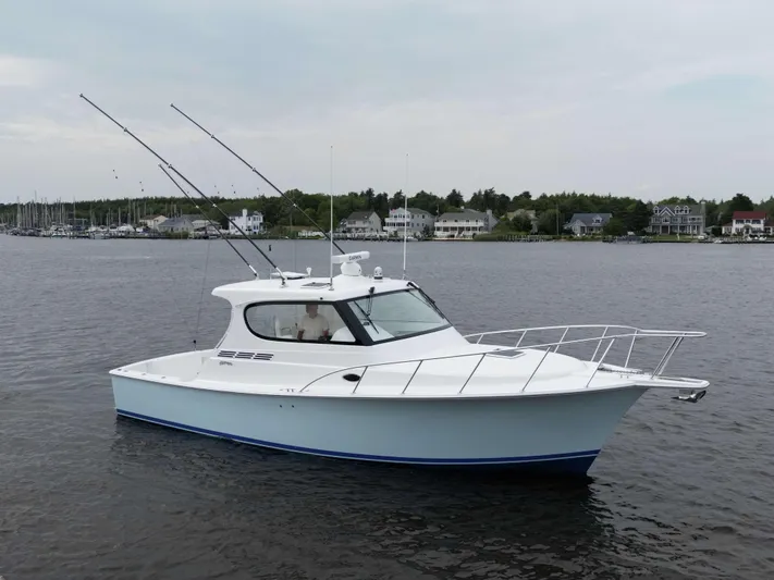  Yacht Photos Pics 2025 Henriques 35 Express Hardtop boat on calm water, with fishing rods and coastal houses in background.