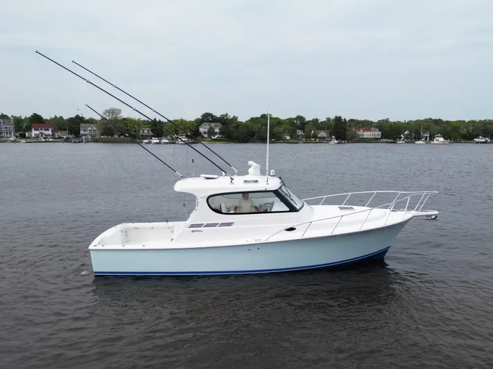  Yacht Photos Pics 2025 Henriques 35 Express Hardtop boat on calm water, with fishing rods, near shoreline.