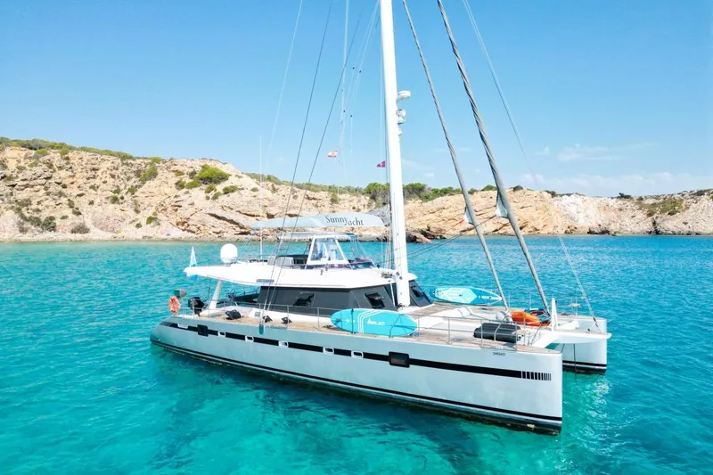 Sunnyacht Yacht Photos Pics 2008 Sunreef 62 catamaran anchored in clear turquoise waters near rocky coastline.