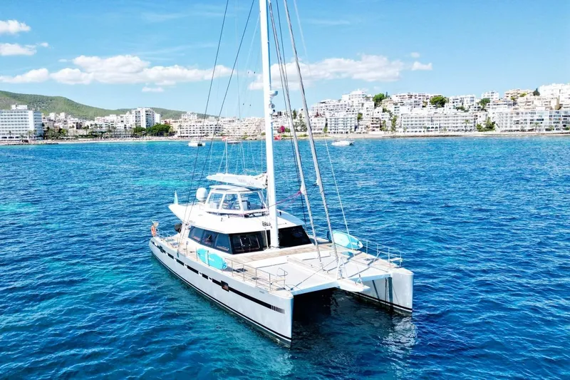 Sunnyacht Yacht Photos Pics Luxurious 2008 Sunreef 62 catamaran sailing on clear blue waters near a coastal city.