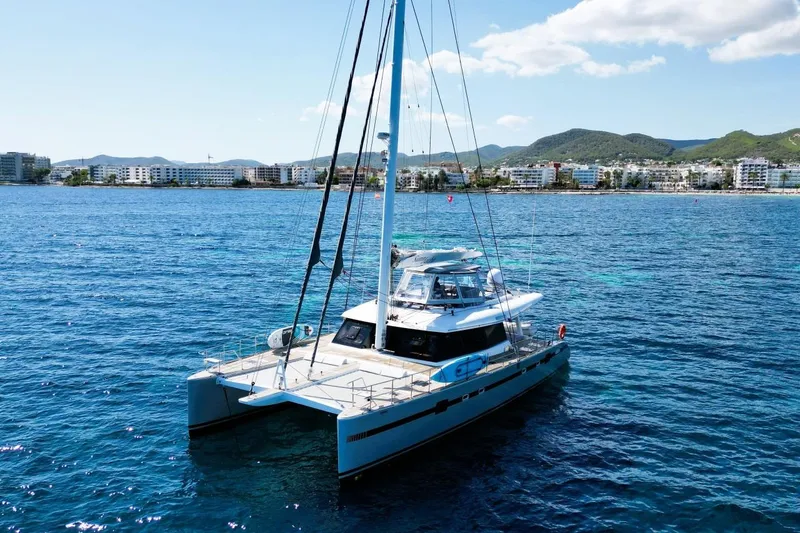 Sunnyacht Yacht Photos Pics 2008 Sunreef 62 catamaran sailing near coastal cityscape, clear blue waters.
