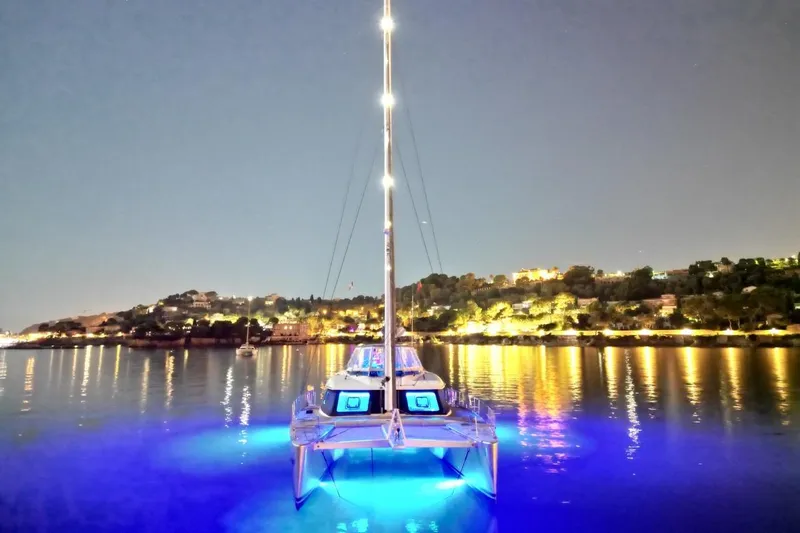 Sunnyacht Yacht Photos Pics 2008 Sunreef 62 catamaran with blue underwater lights, docked at night near illuminated shoreline.