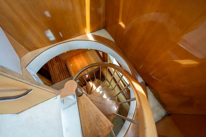 Strictly Business Yacht Photos Pics Spiral staircase inside 2004 Hatteras 65 Enclosed Bridge yacht, featuring elegant wood finish.