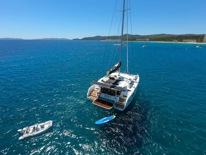 Yoff Yacht Photos Pics 2023 Lagoon 46 catamaran anchored in clear blue sea with paddleboard and dinghy.