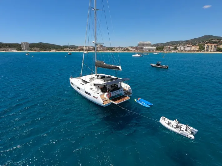 Yoff Yacht Photos Pics 2023 Lagoon 46 catamaran anchored in clear blue water near a coastal city.