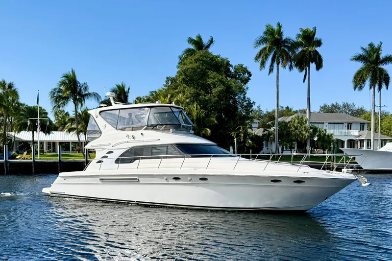  Yacht Photos Pics 1999 Sea Ray 560 Sedan Bridge yacht cruising on a sunny day with palm trees in the background.