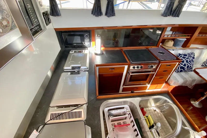 Wonder Yacht Photos Pics 1980 Wellington 44 yacht kitchen with stove, microwave, and sink, featuring wooden cabinetry and modern appliances.