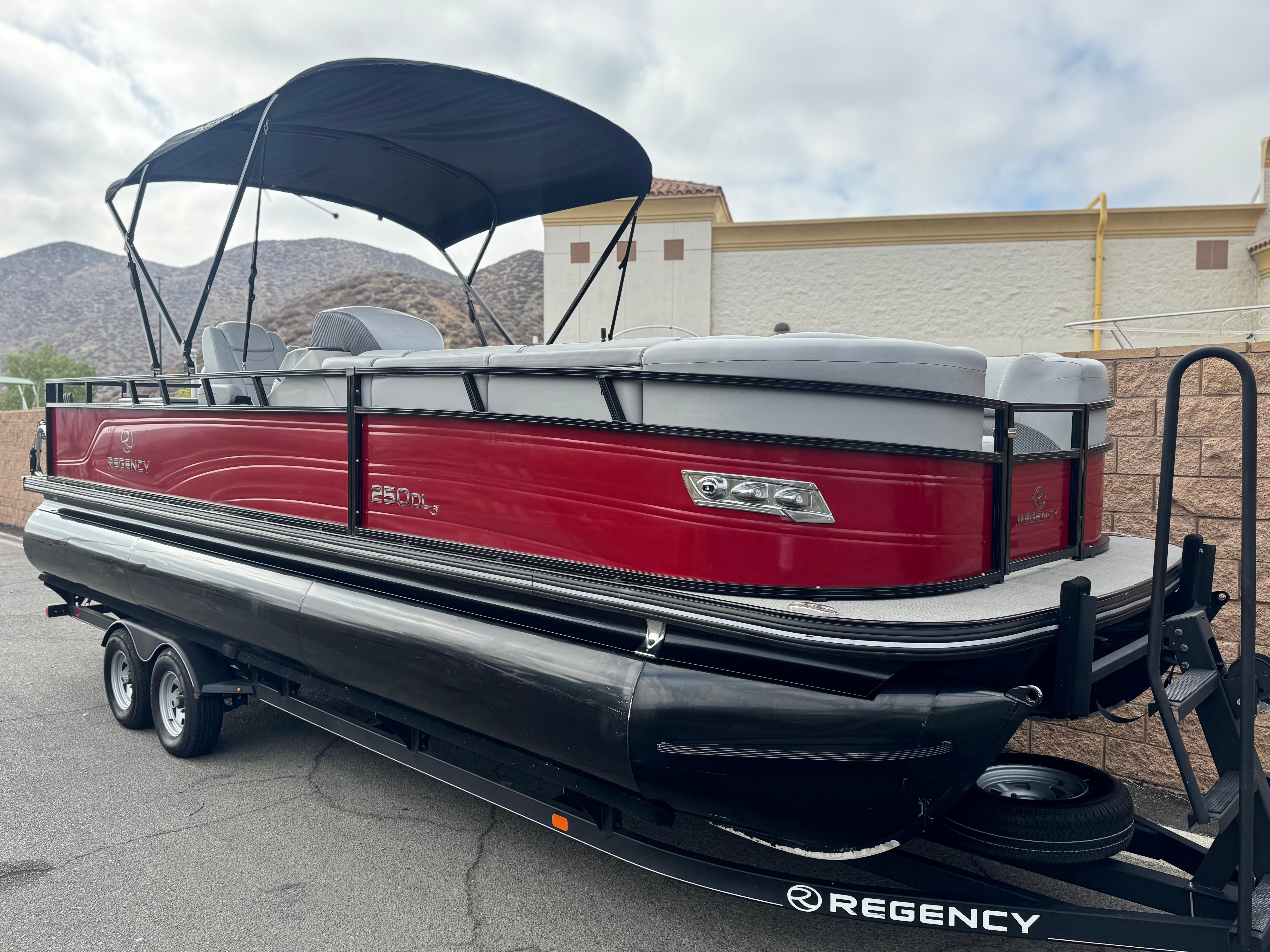 2023 Regency 250 DL3 pontoon boat with red exterior and black canopy on a trailer.