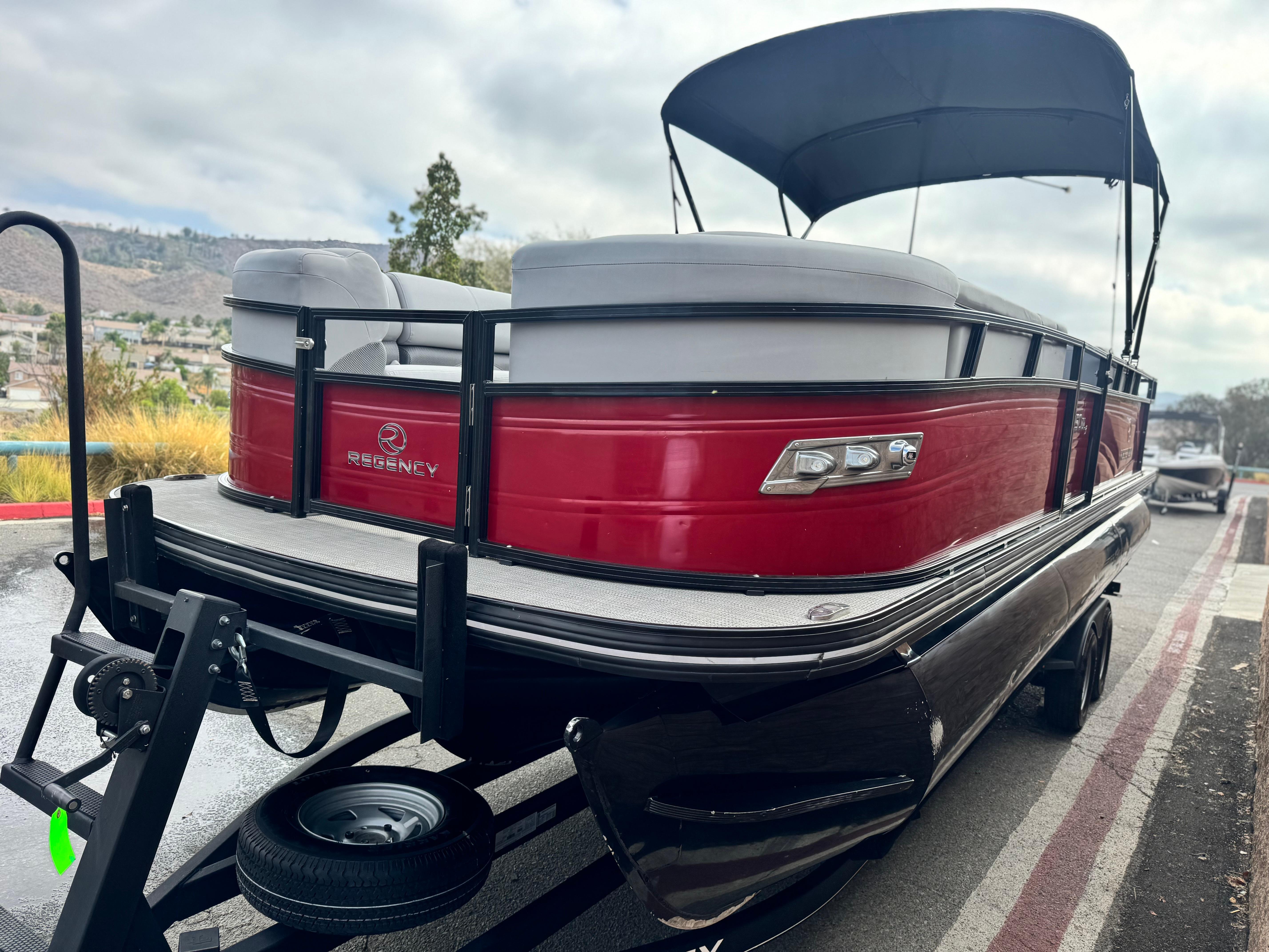 2023 Regency 250 DL3 pontoon boat with red exterior and canopy on trailer.