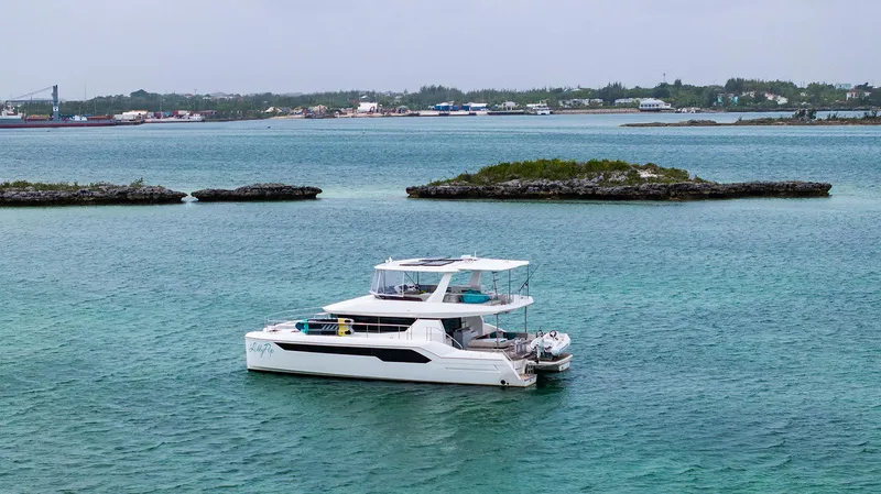 Lollypop Yacht Photos Pics 2022 Leopard 53 Powercat yacht anchored in clear turquoise waters near a rocky shoreline.