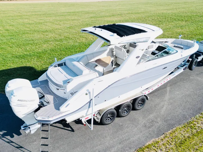 The Good Stuff Yacht Photos Pics 2023 Sea Ray SLX 310 OB boat on trailer, parked on paved surface, grassy background.