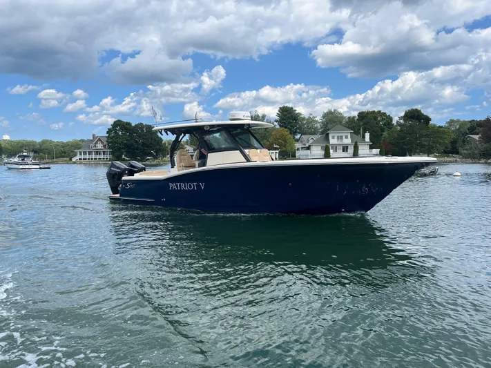  Yacht Photos Pics 2024 Scout 330 LXF boat on water, clear sky, waterfront homes in background.