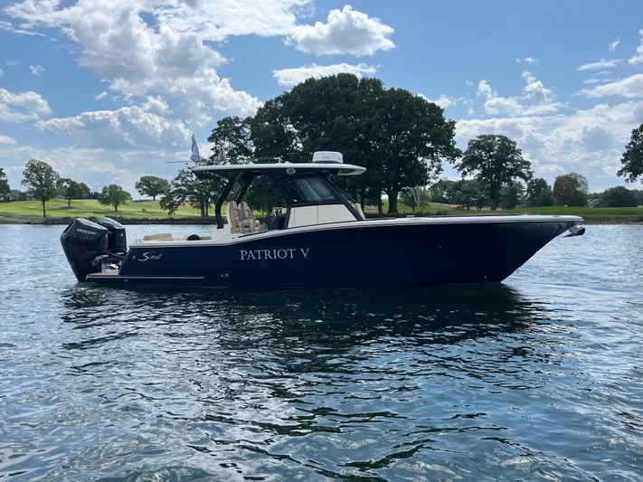  Yacht Photos Pics 2024 Scout 330 LXF boat on a lake with trees in the background.