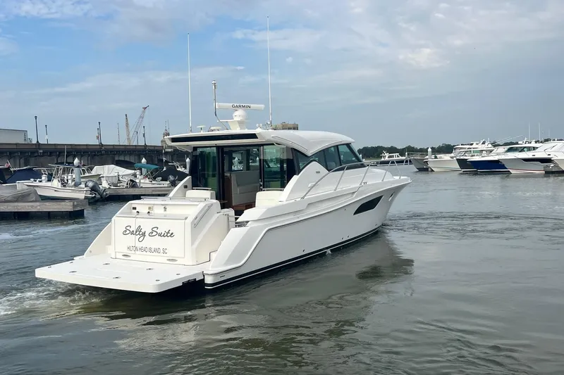 Salty Suite Yacht Photos Pics 2023 Tiara Yachts C44 Coupe cruising in a marina, rear view.