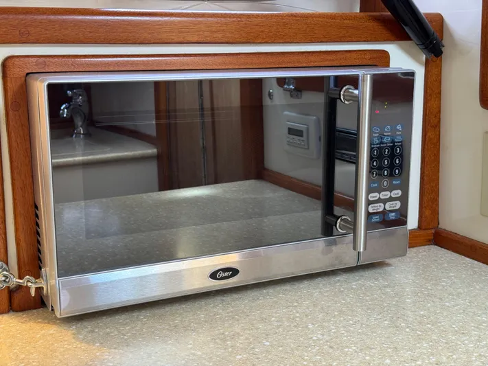 Wrecking Crew Yacht Photos Pics Stainless steel Oster microwave on a boat's kitchen counter, surrounded by wood trim.