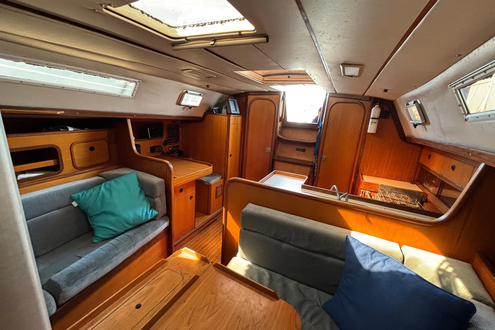 Interior of 1986 Beneteau First 375 sailboat, featuring cozy seating and wooden cabinetry.