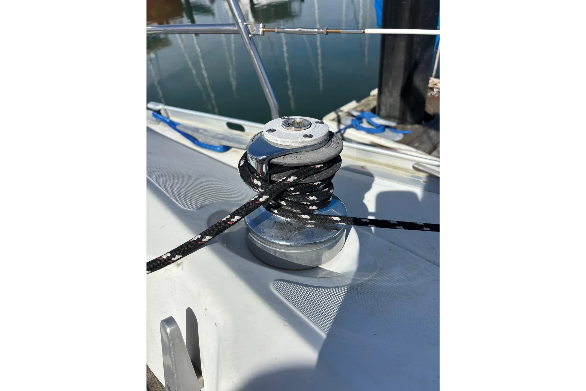 Winch on 1986 Beneteau First 375 sailboat deck with rope, docked in marina.