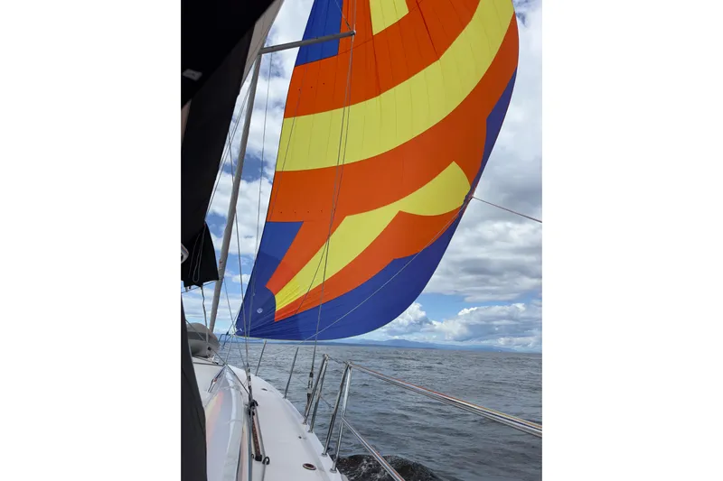 Lost Traveler Yacht Photos Pics Jeanneau Sun Odyssey 440 sailboat with colorful spinnaker, 2020 model, sailing on open water.