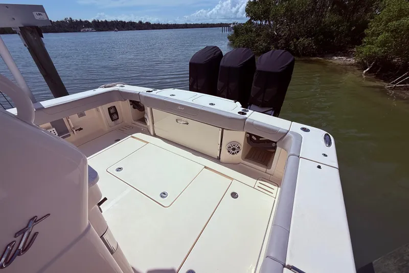  Yacht Photos Pics 2022 Scout 425 LXF boat deck with triple outboard motors, docked by a scenic shoreline.