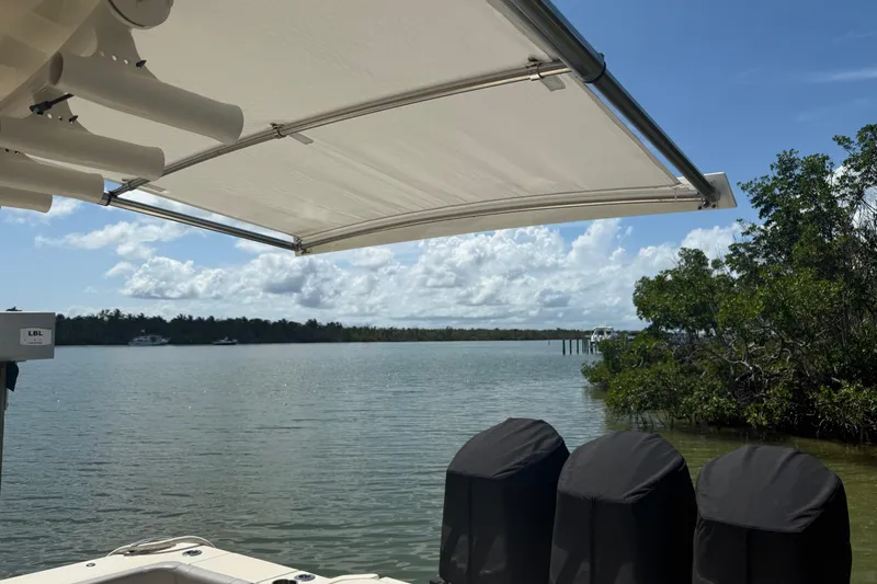  Yacht Photos Pics 2022 Scout 425 LXF boat with canopy, overlooking serene water and lush greenery.