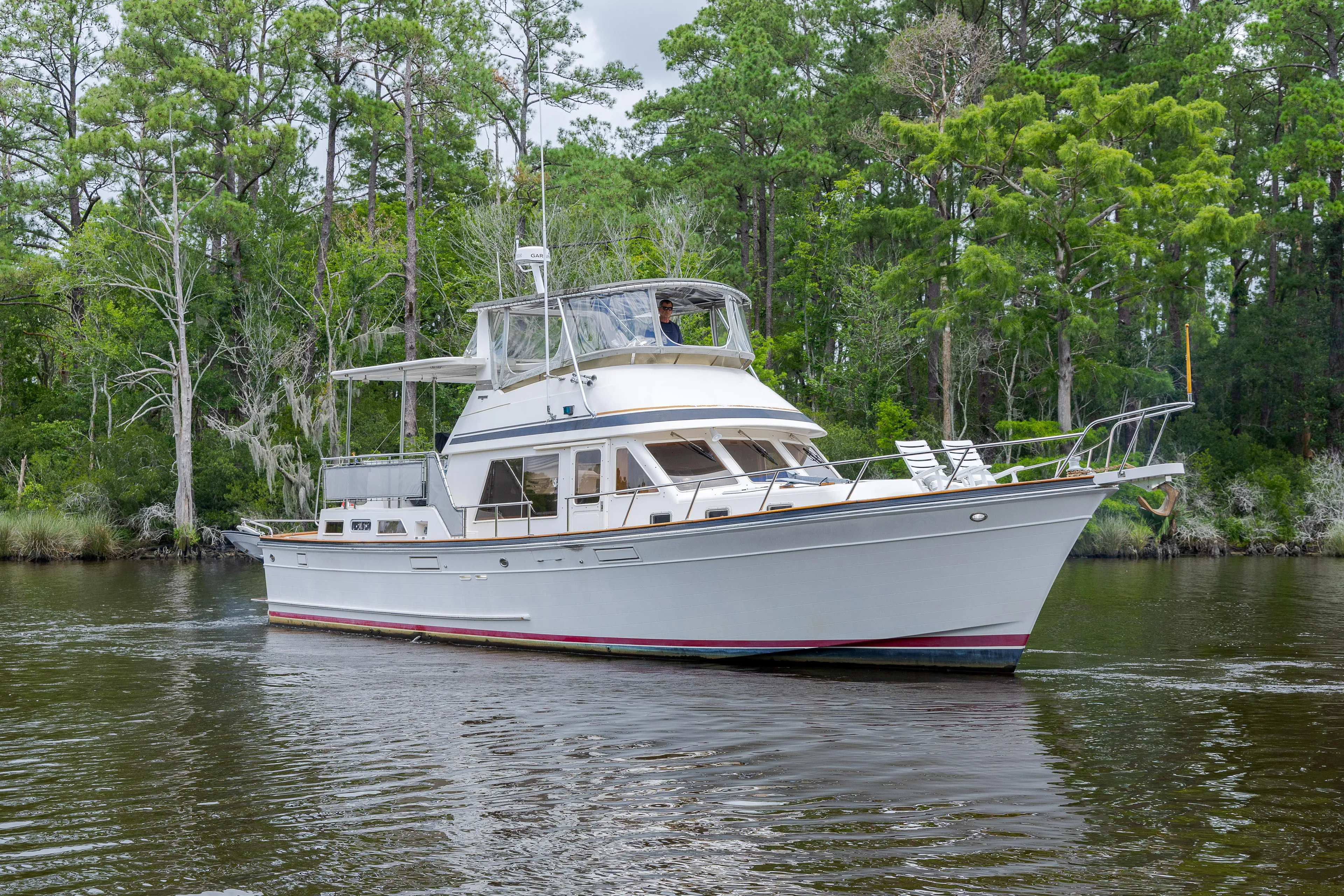  Yacht Photos Pics 1989 Offshore Yachts 48 Yachtfisher cruising on a serene river, surrounded by lush greenery.