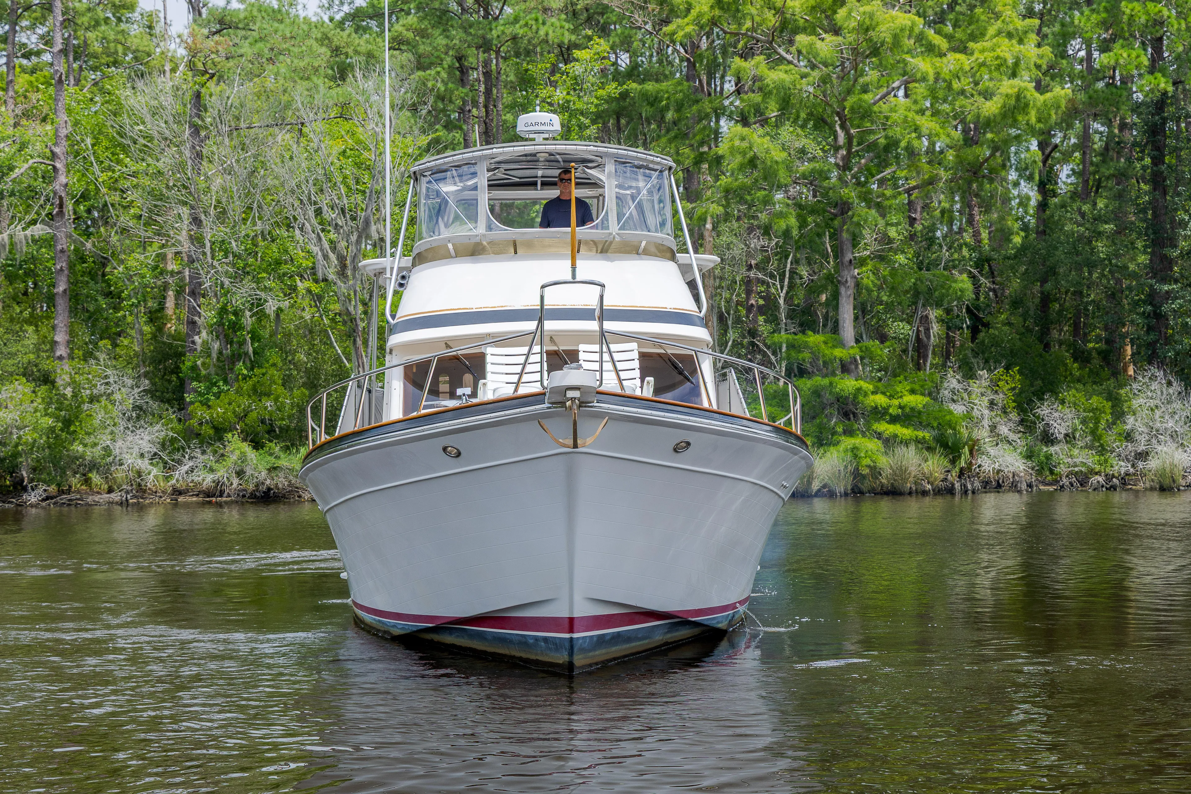  Yacht Photos Pics 1989 Offshore Yachts 48 Yachtfisher cruising on a serene river, surrounded by lush greenery.